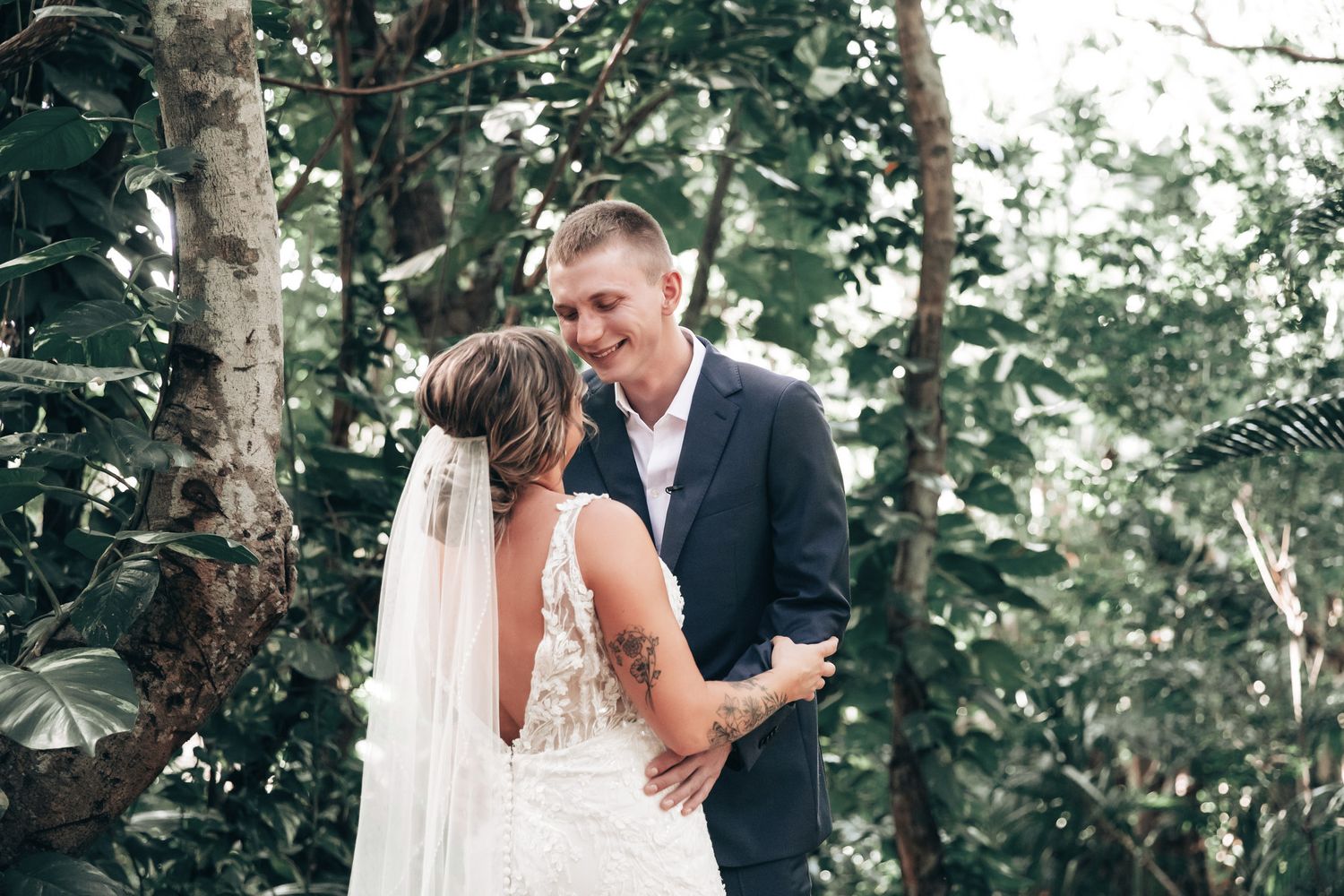 Bride and groom share an intimate moment surrounded by lush tropical greenery on their wedding day.