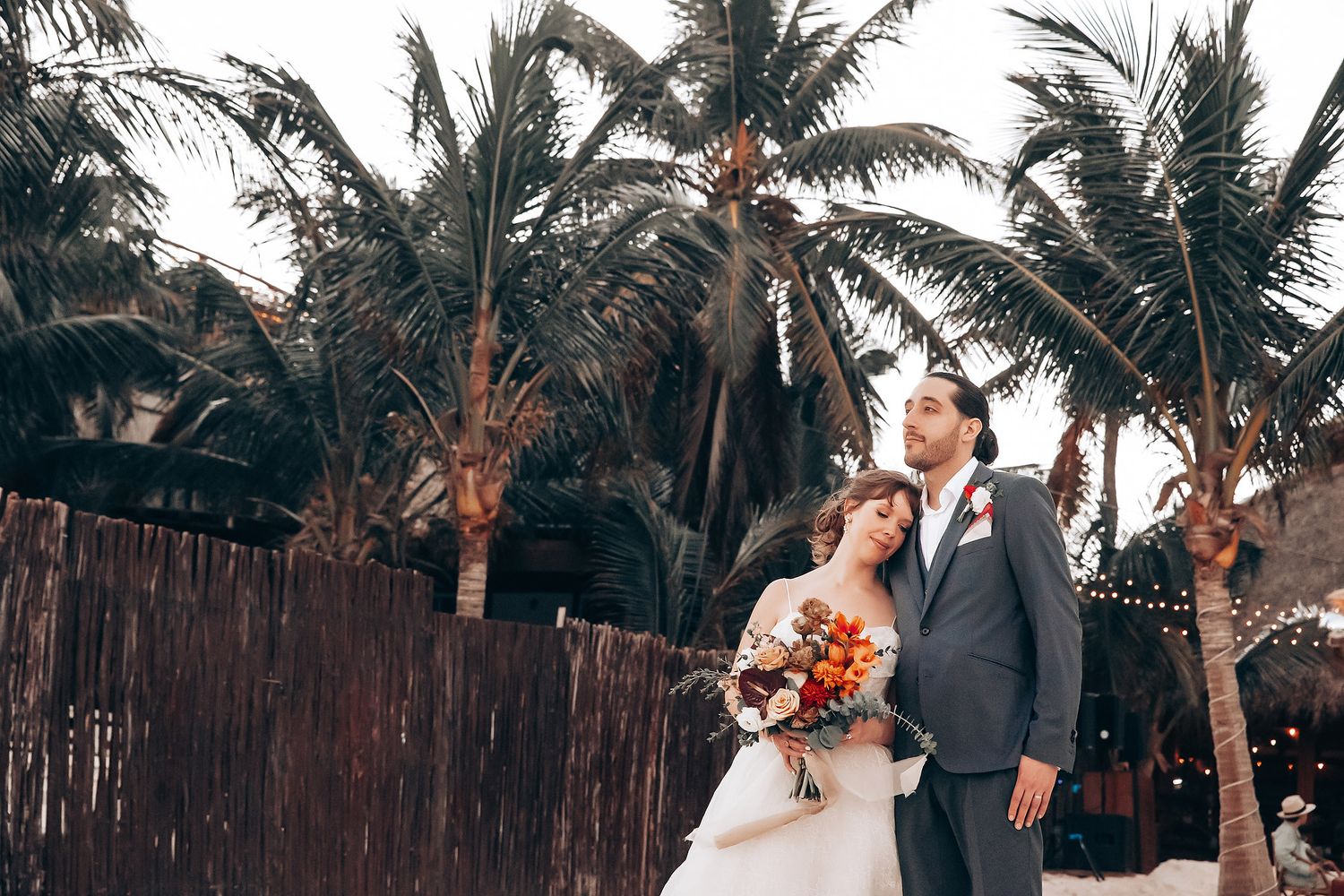 Wedding couple posing in front of tropical palm trees at a beach resort.