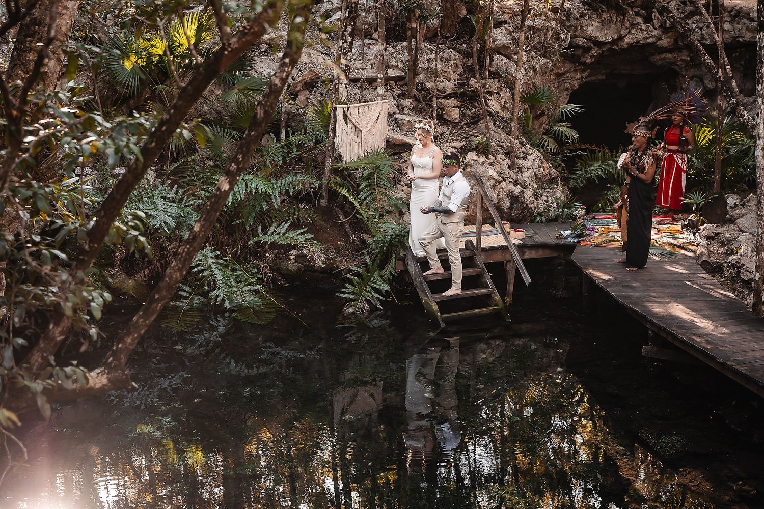Couple exchanges vows on a wooden dock over a serene jungle cenote surrounded by lush tropical greenery.