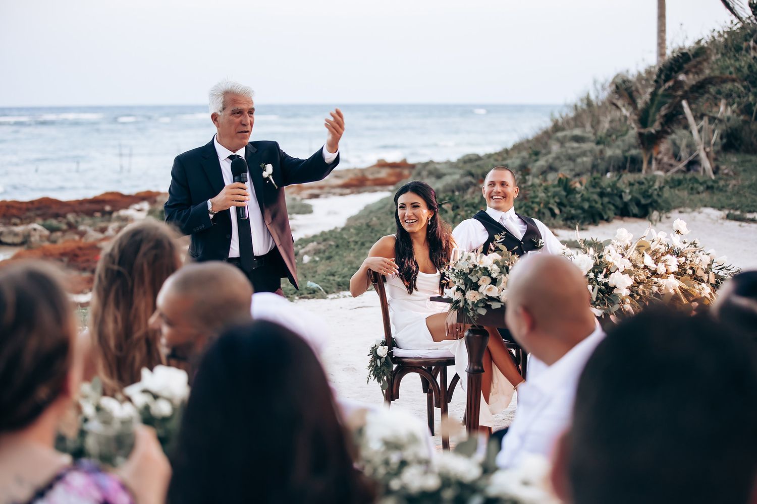 A seaside wedding ceremony with white floral arrangements and natural coastal vegetation.