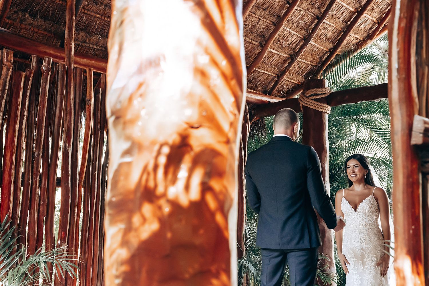 Wedding ceremony setup with wooden chairs and floral arrangements under a rustic bamboo canopy on a tropical beach.