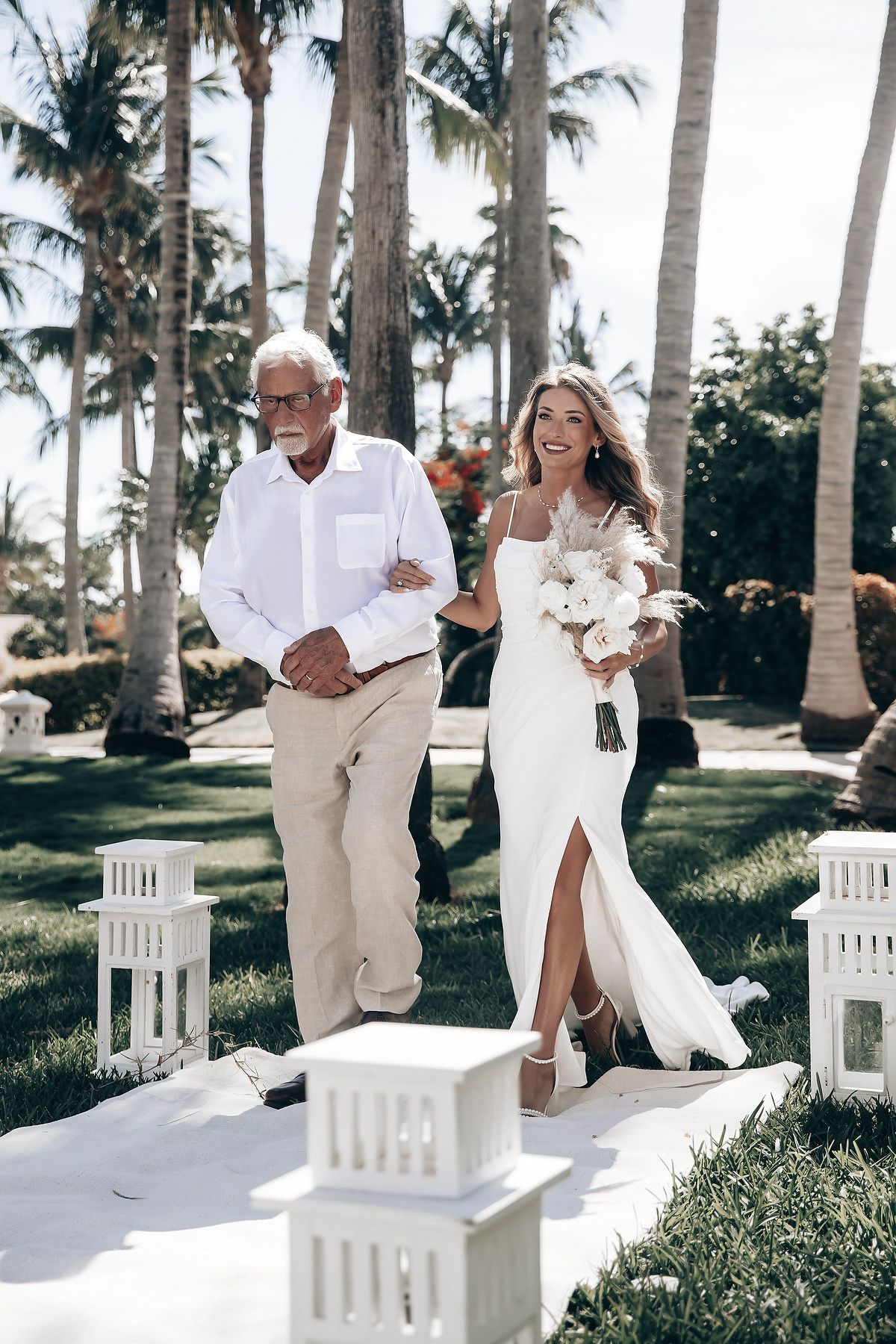 A bride and groom walk together on a path surrounded by palm trees.