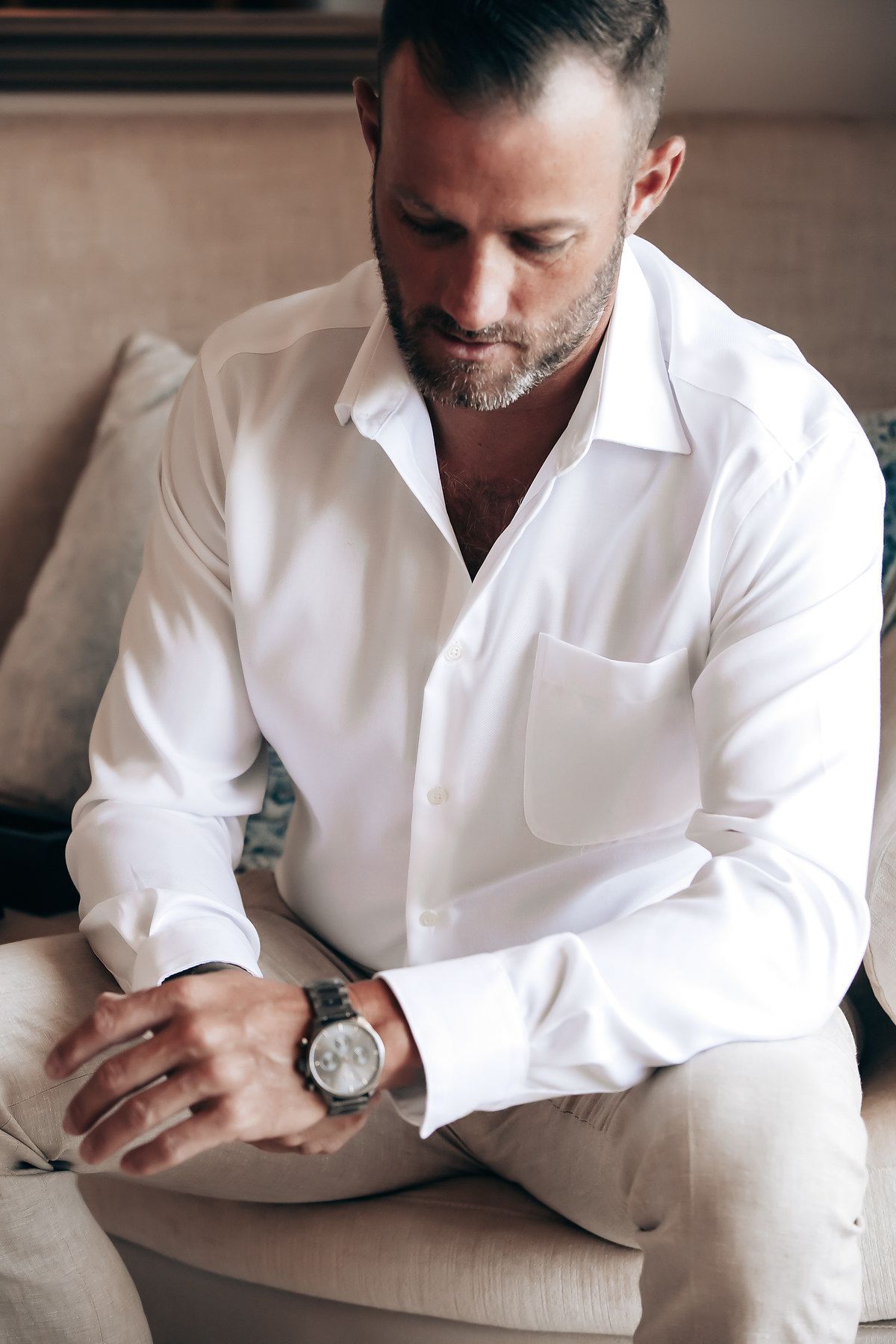 A man in a white shirt sitting on a couch and looking down.