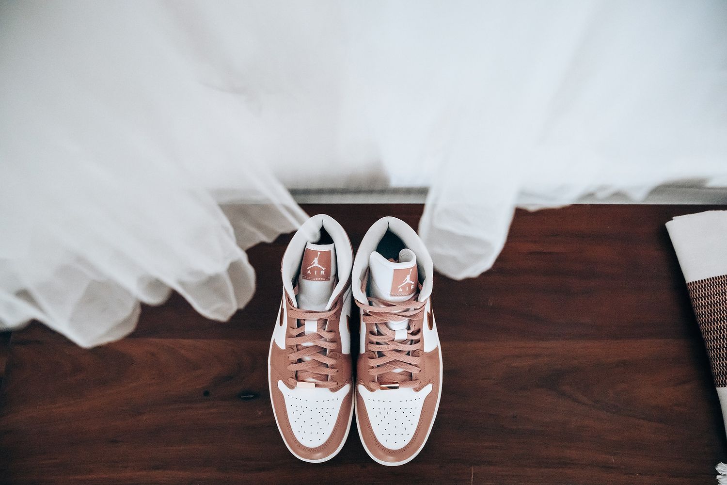A pair of white and pink sneakers sit on a wooden surface.