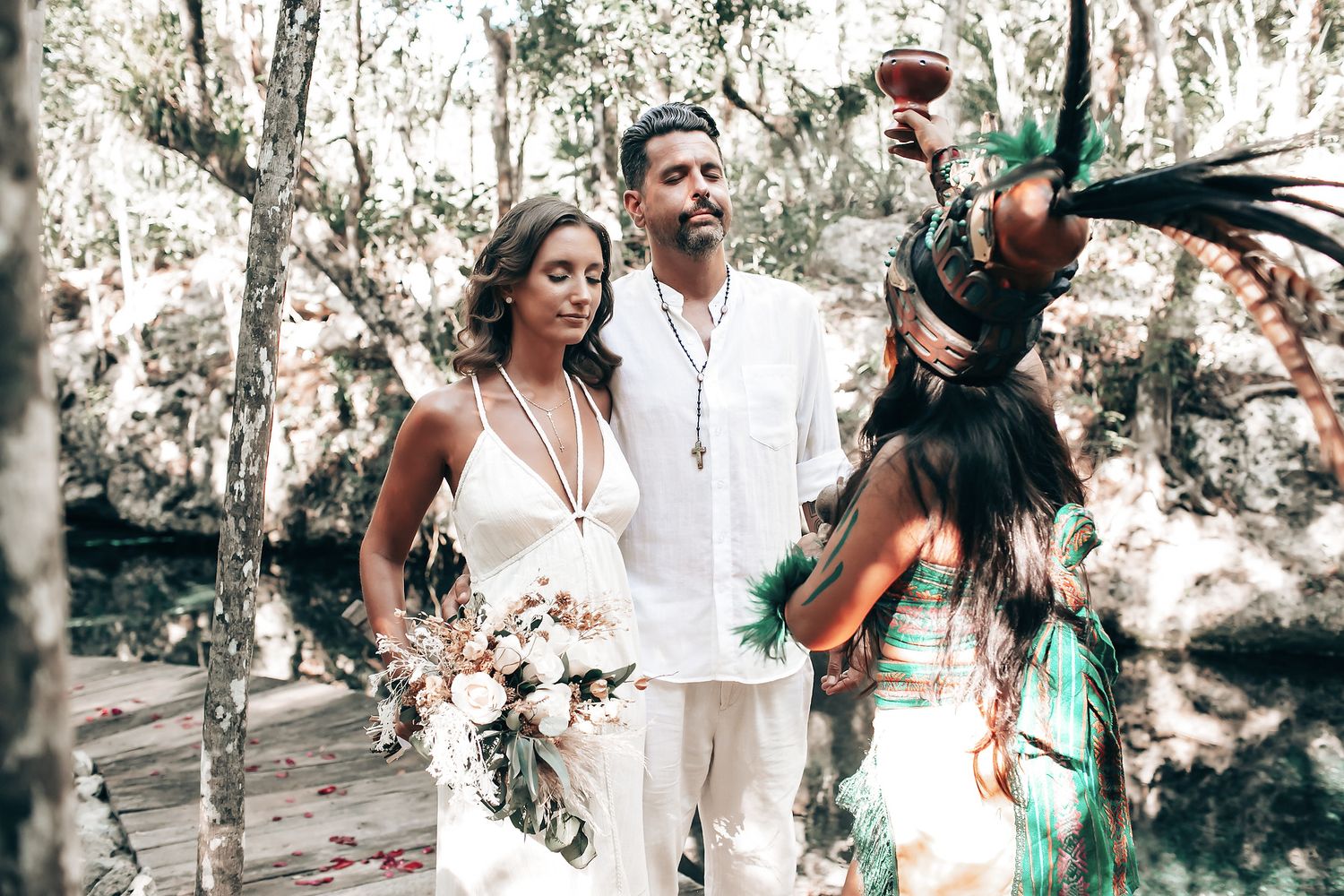 A couple dressed in formal attire walking together in a lush, forested setting.