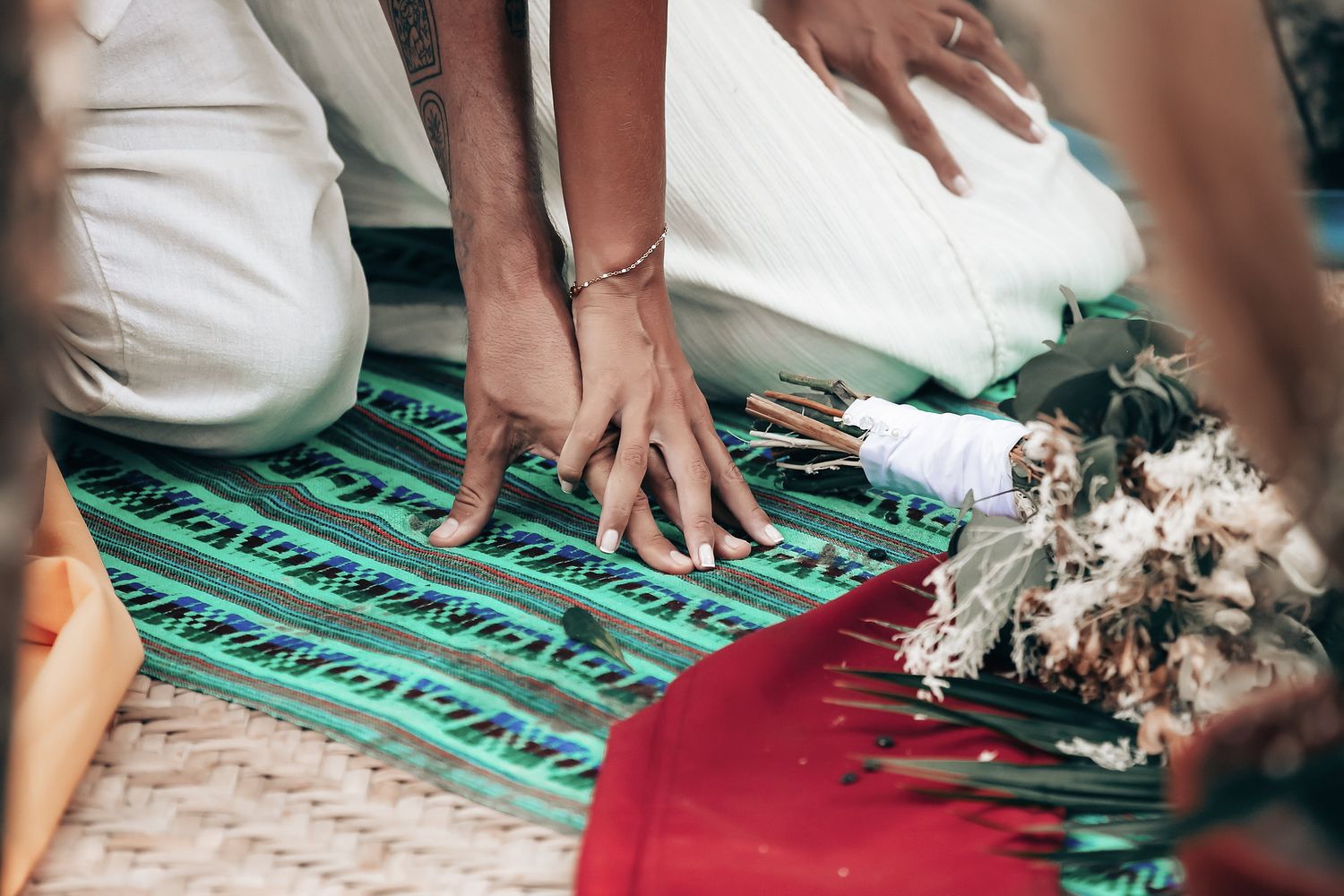 Two people's hands are arranging flowers on a colorful patterned rug.