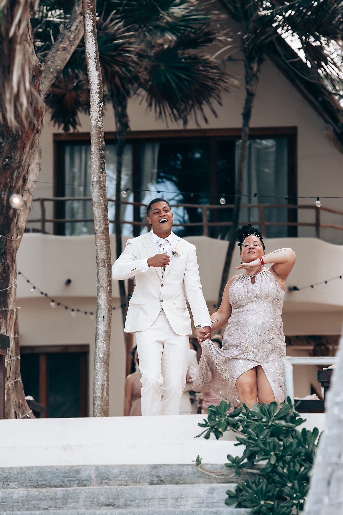 Wedding celebration on a palm-lined terrace with guests in white attire enjoying the festivities.