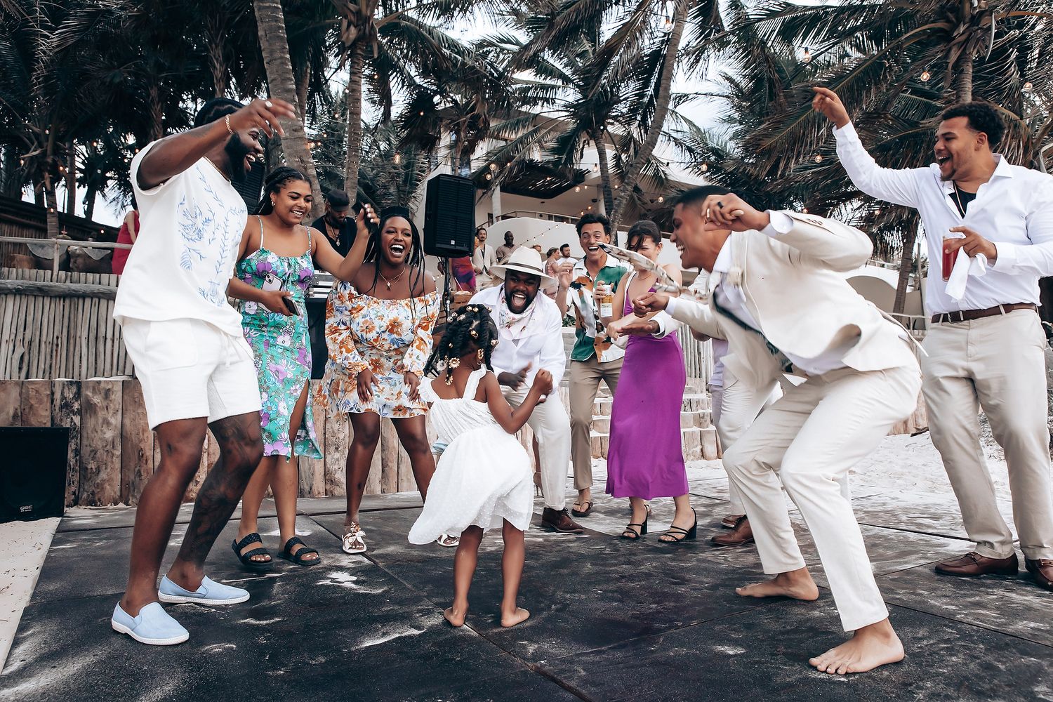 Wedding guests dancing and celebrating at a beach reception in white attire.