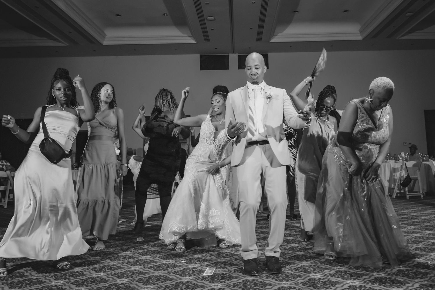 Groom dances joyfully with wedding guests in elegant ballroom during lively wedding reception celebration.