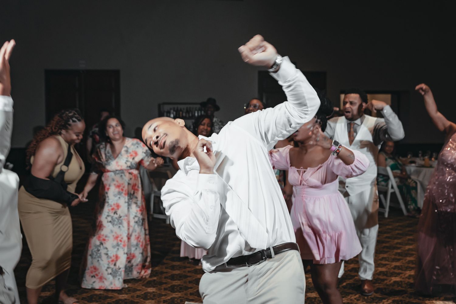 Guests dancing energetically at a wedding reception, with a bald man in a white shirt striking a dramatic pose on the dance floor.