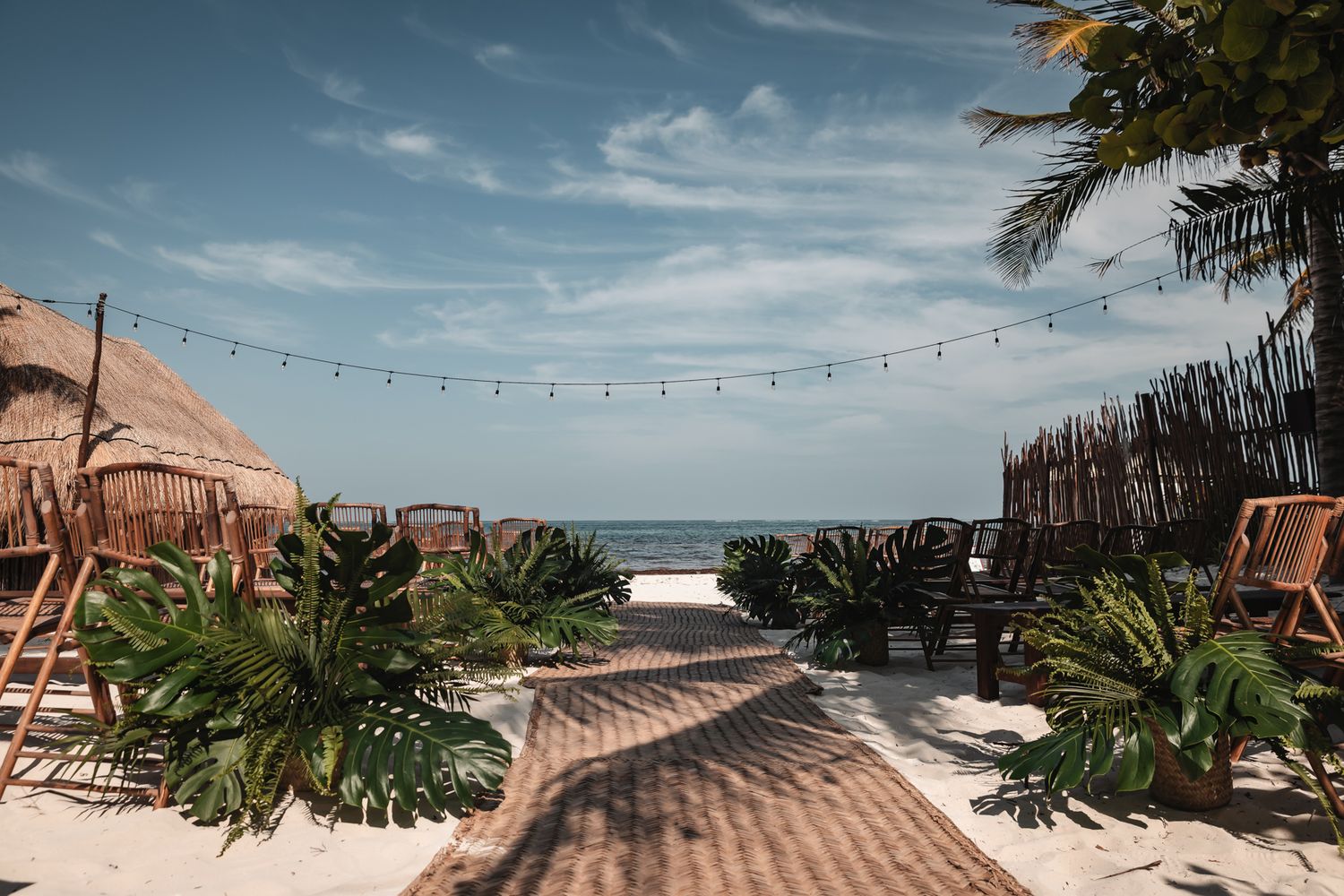 Tropical beach pathway with hammock, palm trees, string lights, and ocean view at a resort.