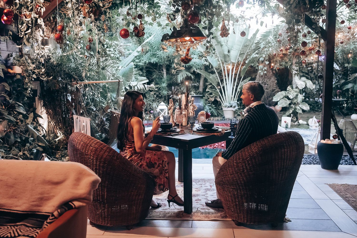 Man and woman enjoying an intimate dinner at a beautifully decorated indoor garden restaurant with holiday ornaments.