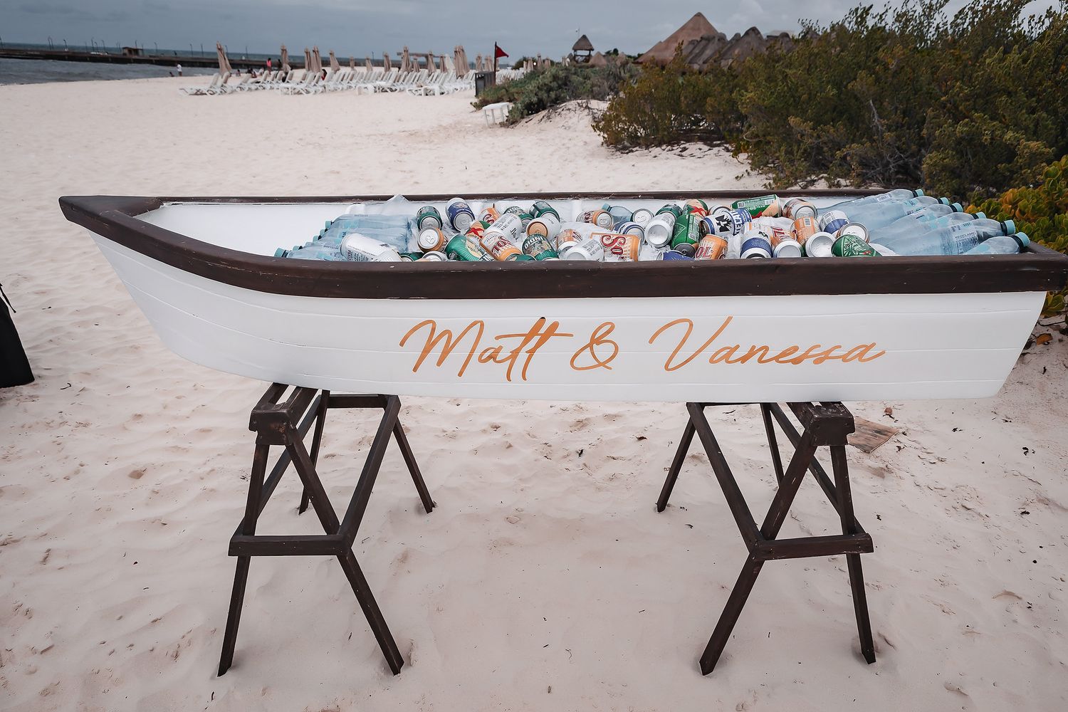 White boat cooler filled with beverages on a sandy beach, personalized with Matt & Vanessa in elegant script lettering.