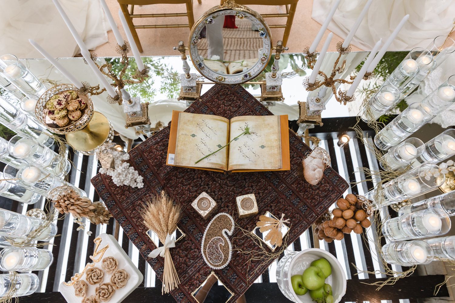 Overhead view of an elegant Persian Sofreh Aghd wedding table with an open book, candles, and traditional decorative items.