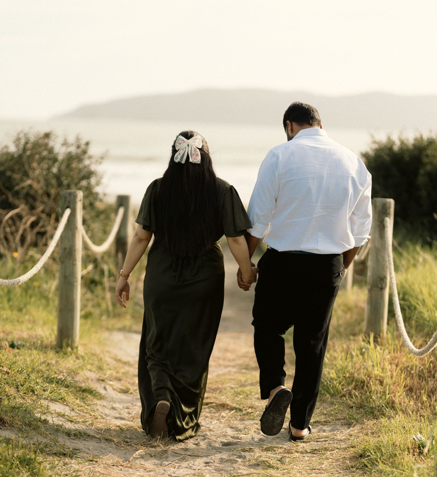 Two people walking together on a path at sunset with rope barriers.