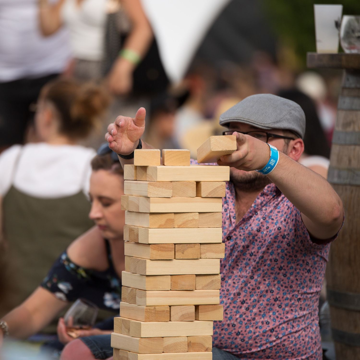 Person carefully removing block from giant Jenga tower at outdoor event.