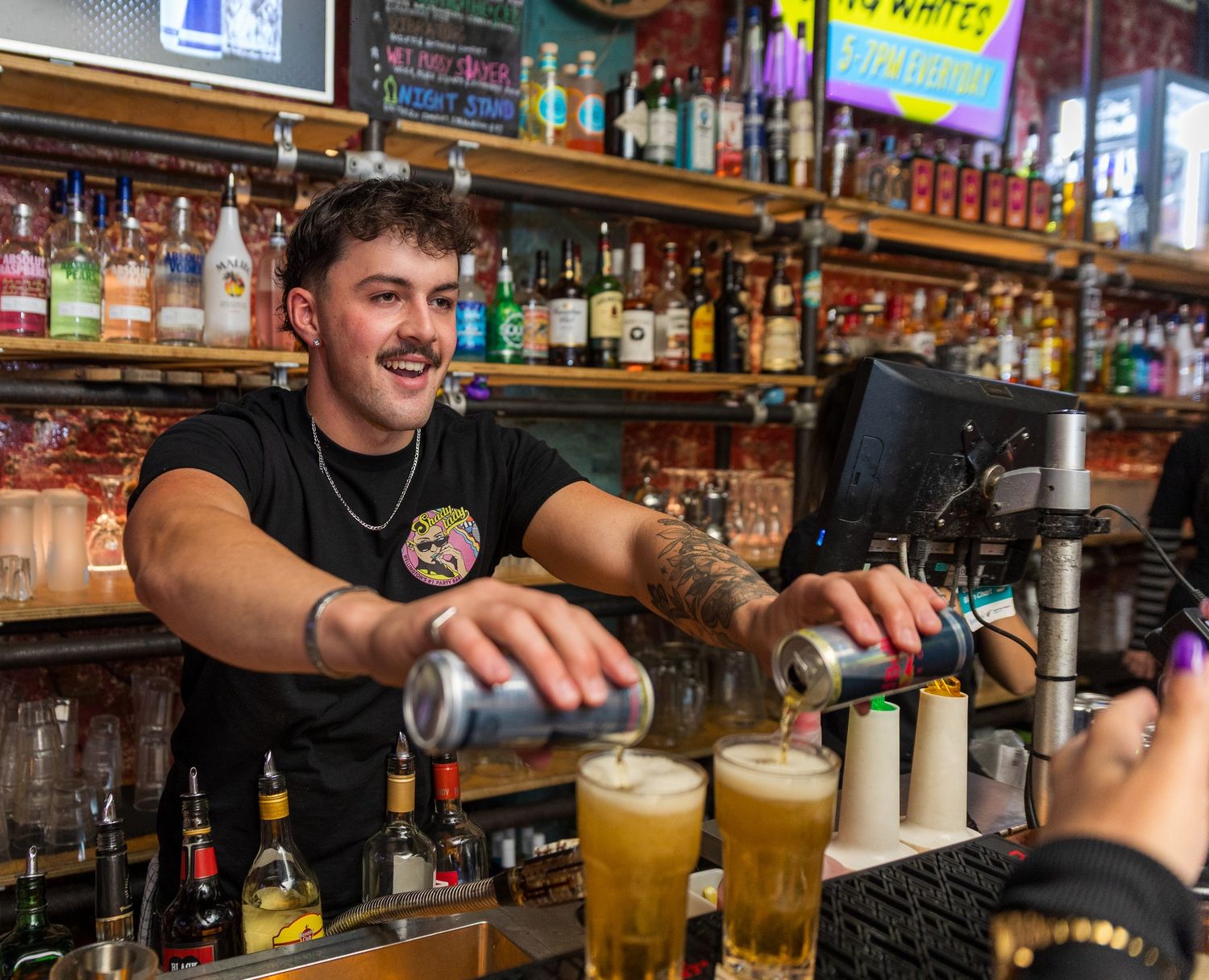 Busy bar scene with bartenders pouring drinks and serving customers at a well-stocked establishment.