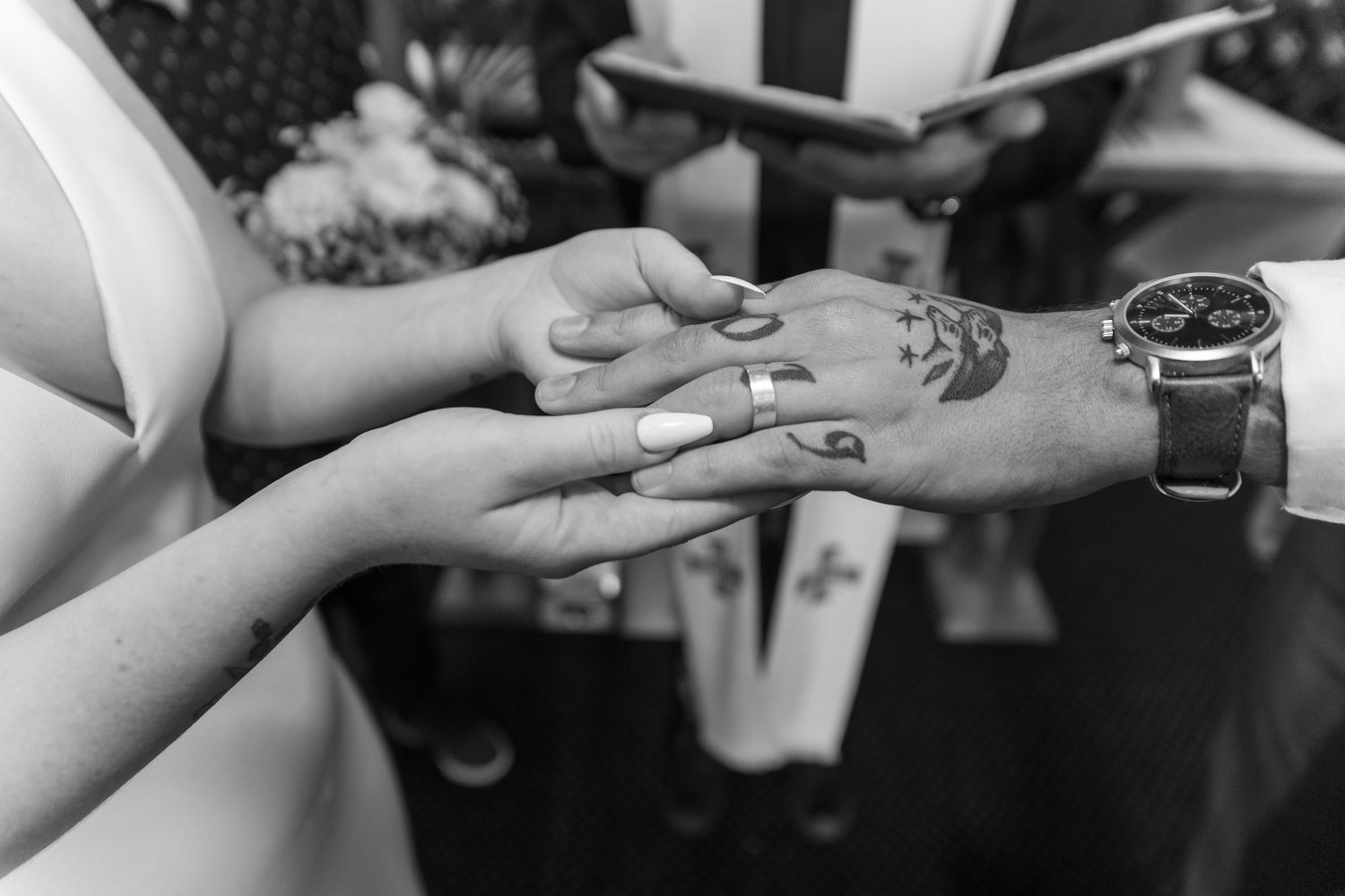 Black and white photograph capturing the intimate moment of a ring exchange during a wedding.