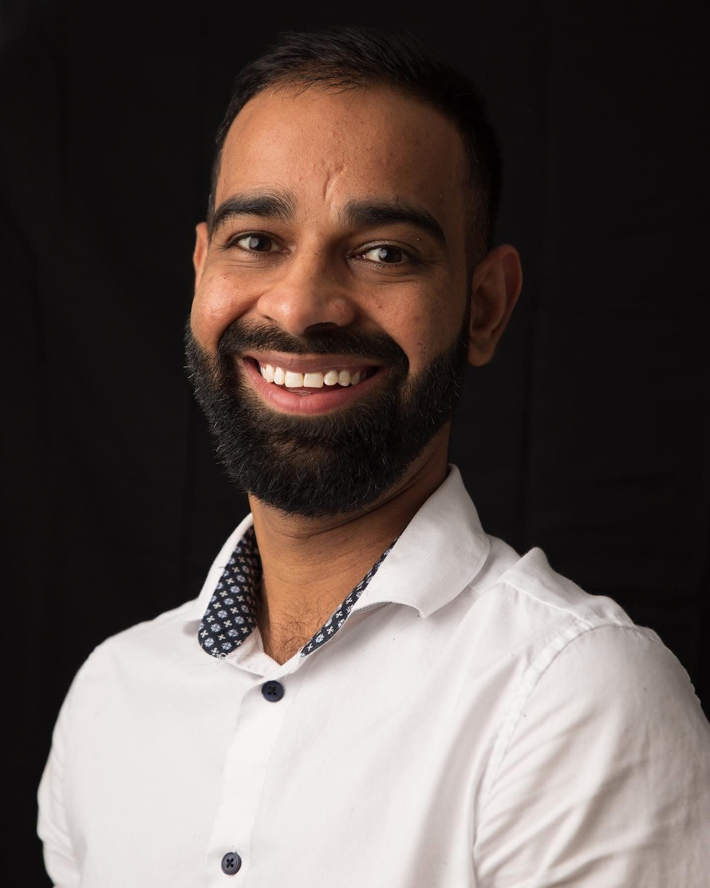 Professional headshot against black background showing warm smile.