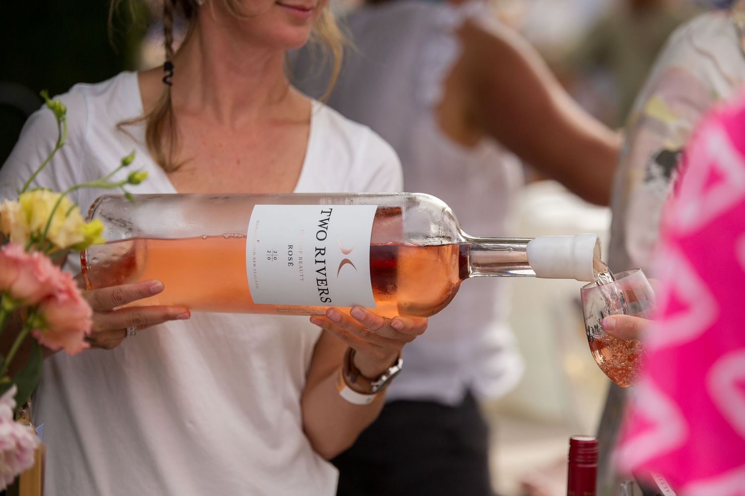 Someone pouring rose wine into glasses at an outdoor gathering with flowers.