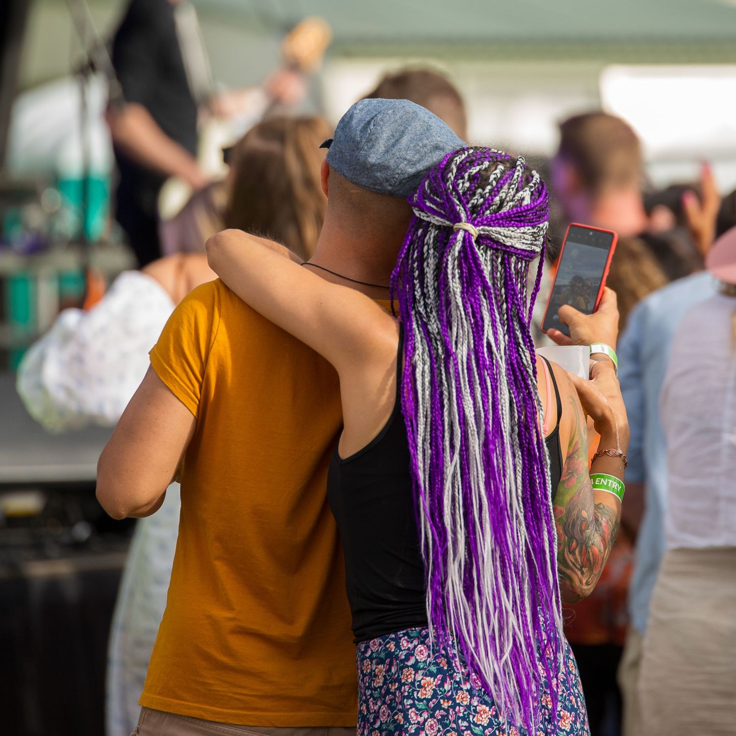 Festival-goer with striking purple and white braided hair embracing another attendee.