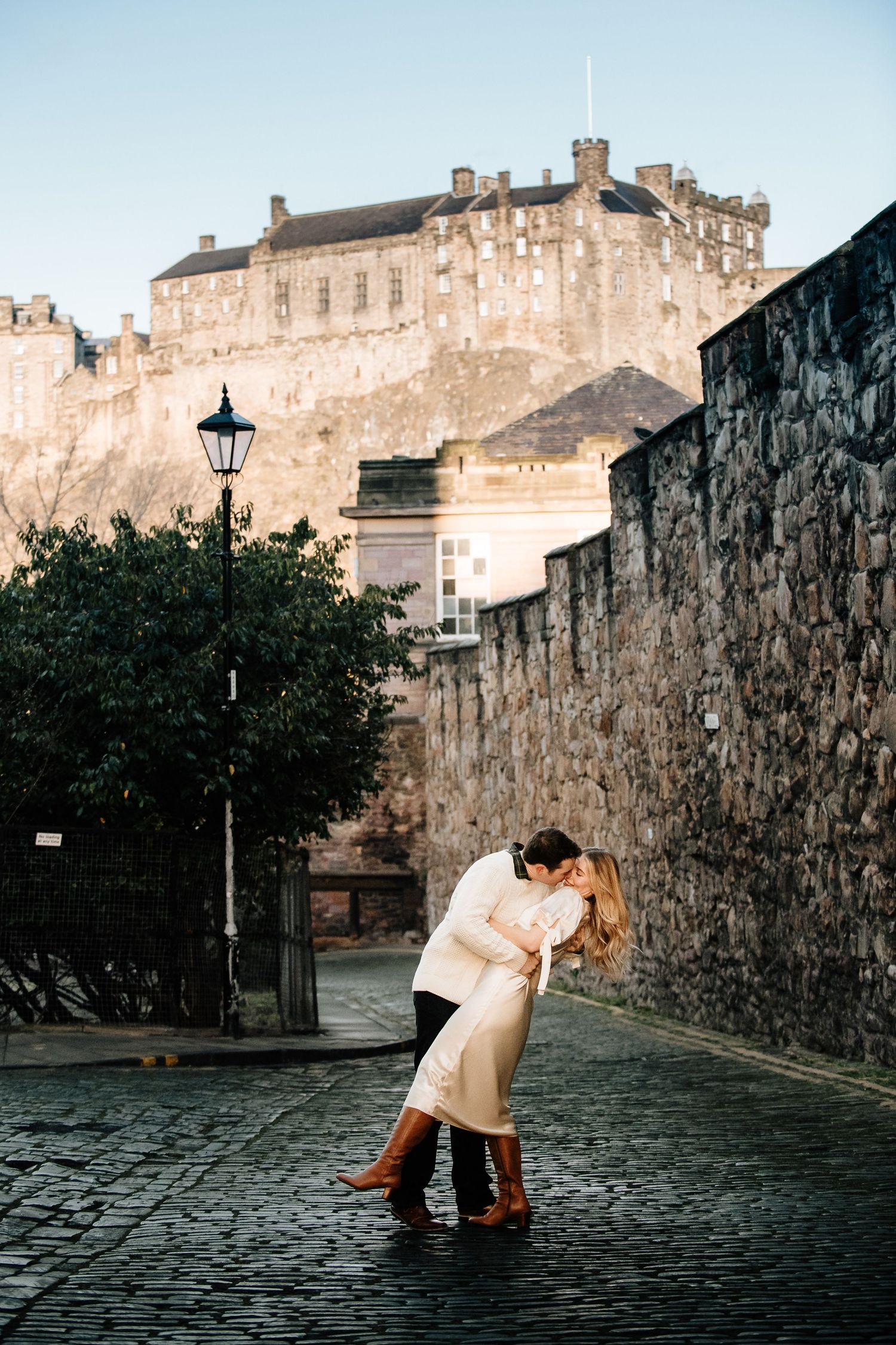 Dramatic dip pose on cobblestone street with Edinburgh Castle looming in background.