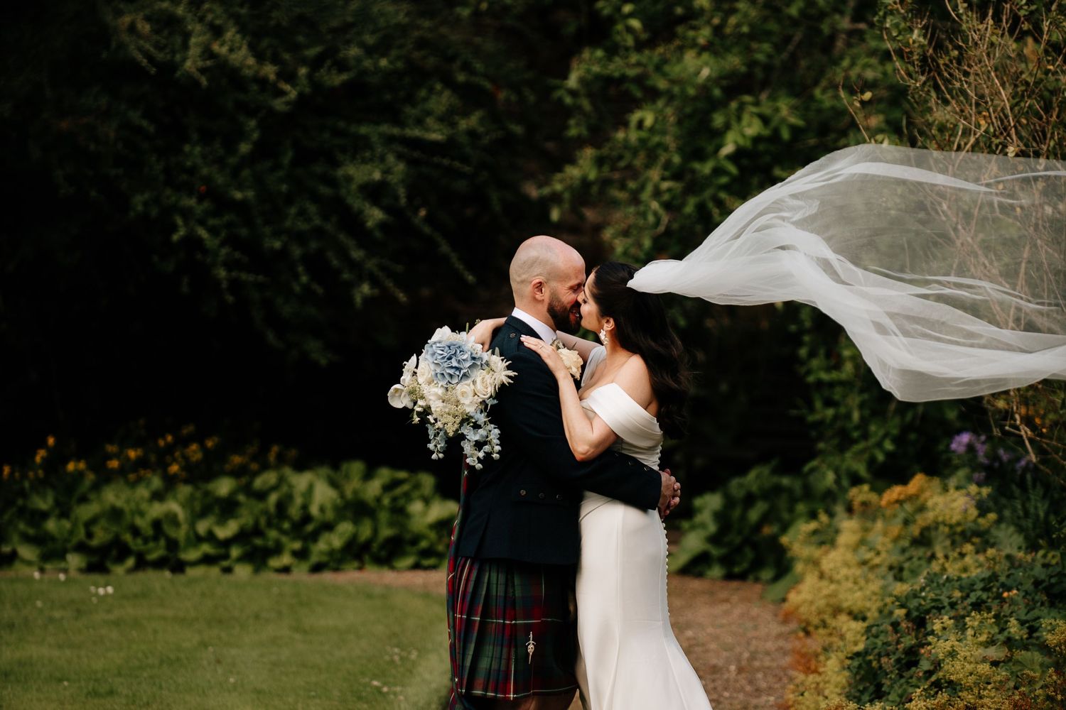 Wedding couple embracing in a scenic garden with flowing veil.