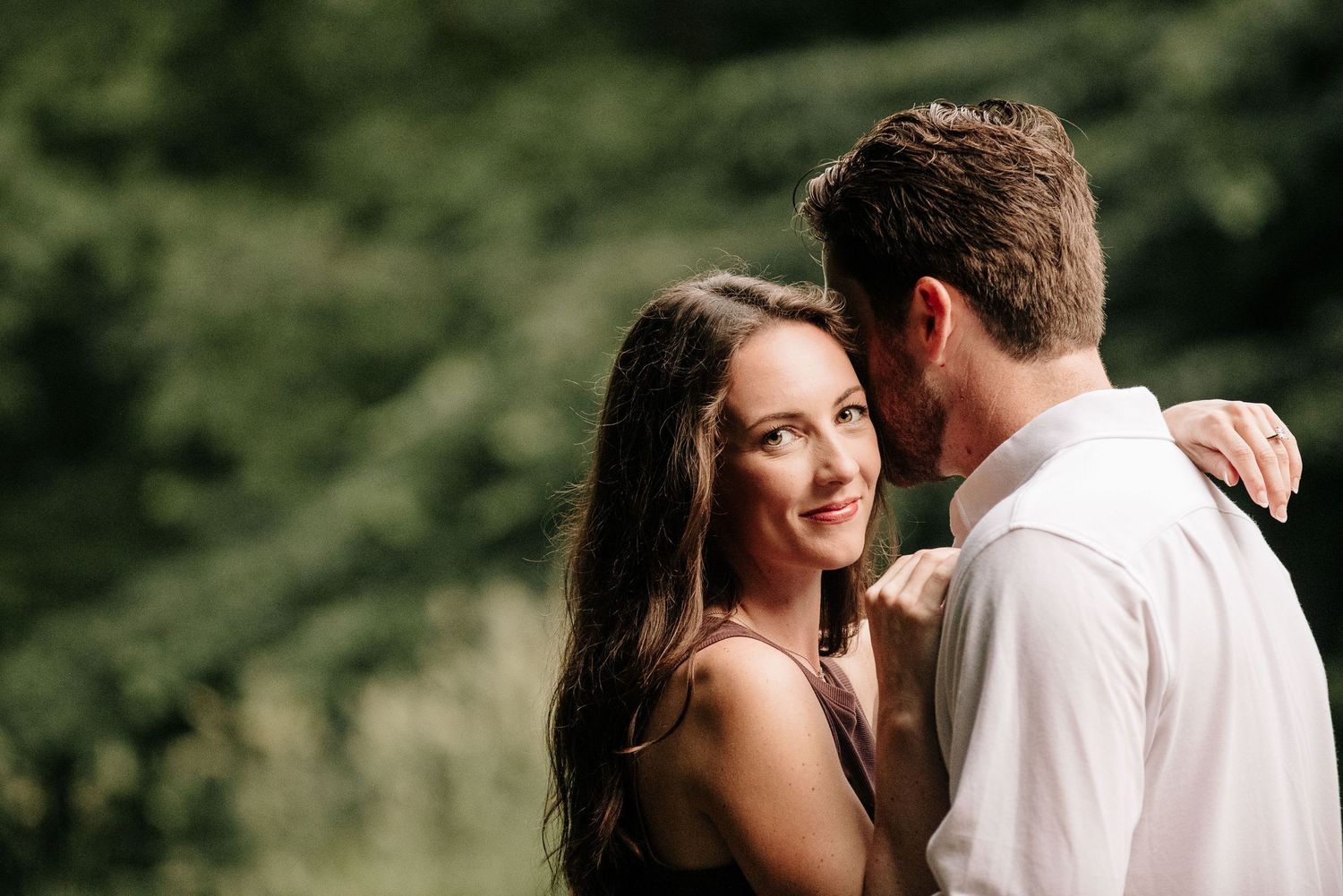 A romantic couple embraces in an outdoor setting with soft natural lighting.