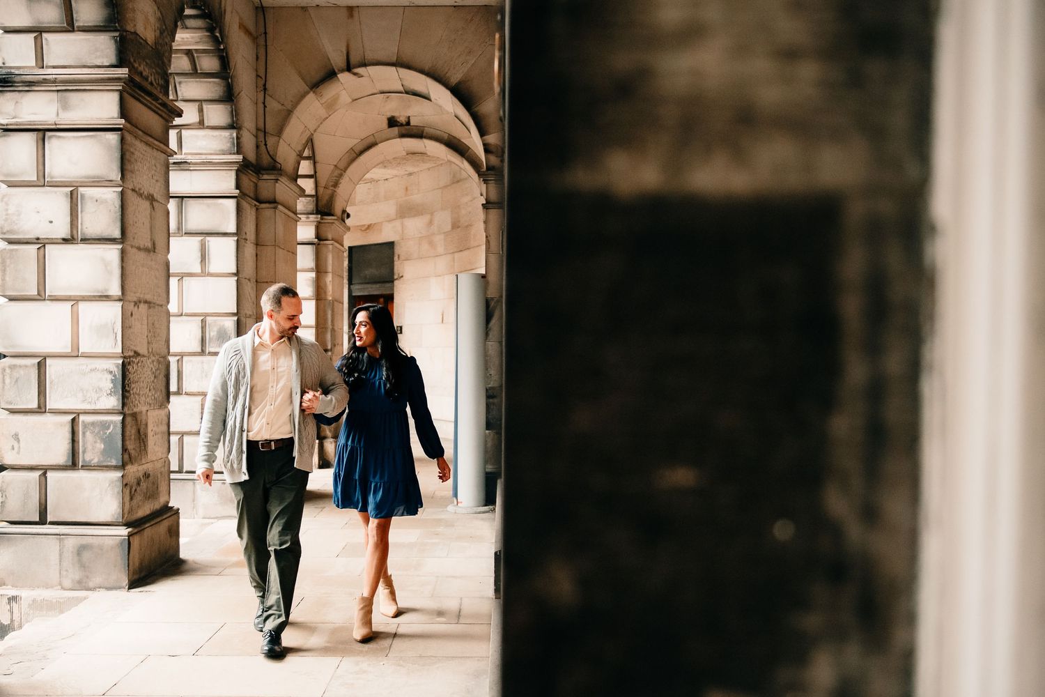 People walking through a historic stone archway corridor with dramatic lighting and architectural details.