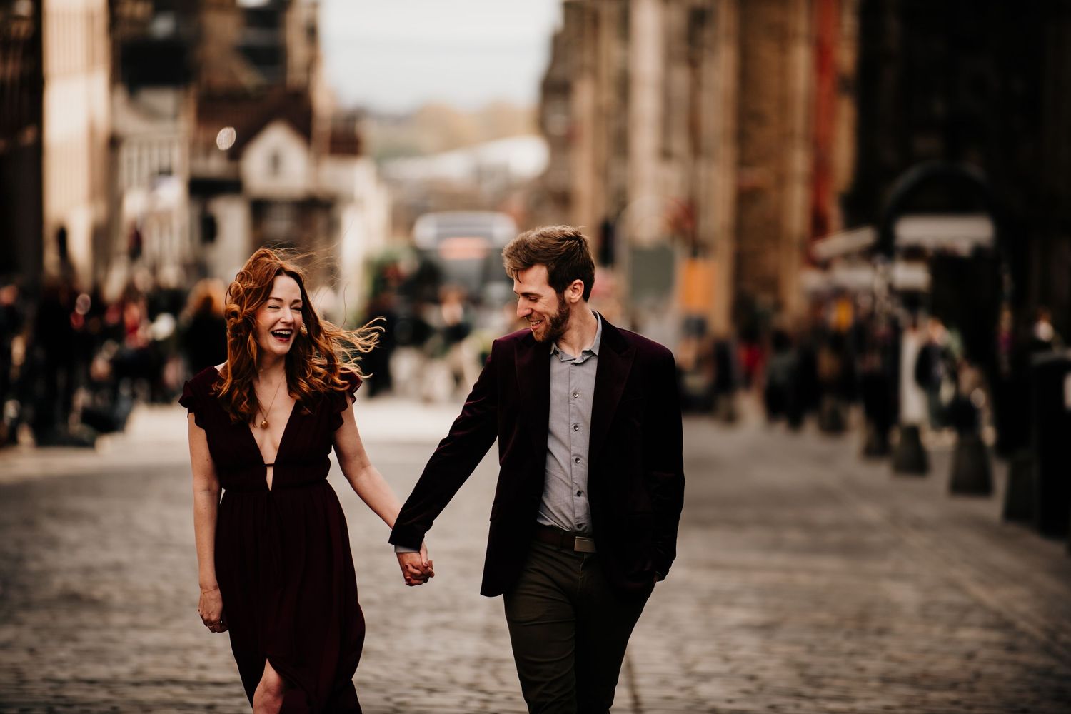 Couple walking hand in hand down a cobblestone street in Edinburgh during golden hour.
