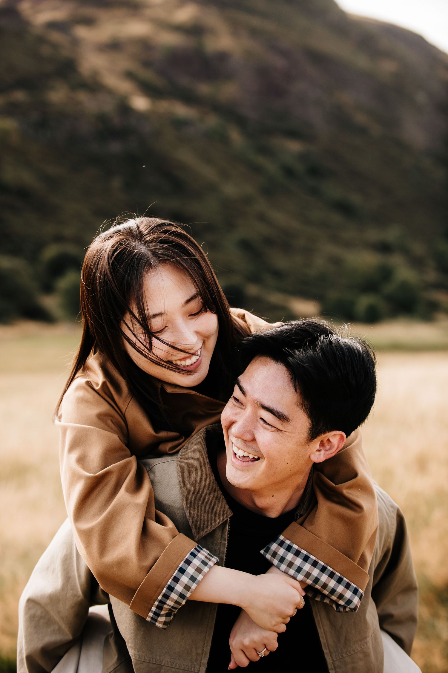 A romantic couple embraces in a golden field during sunset wearing matching tan and plaid outfits.