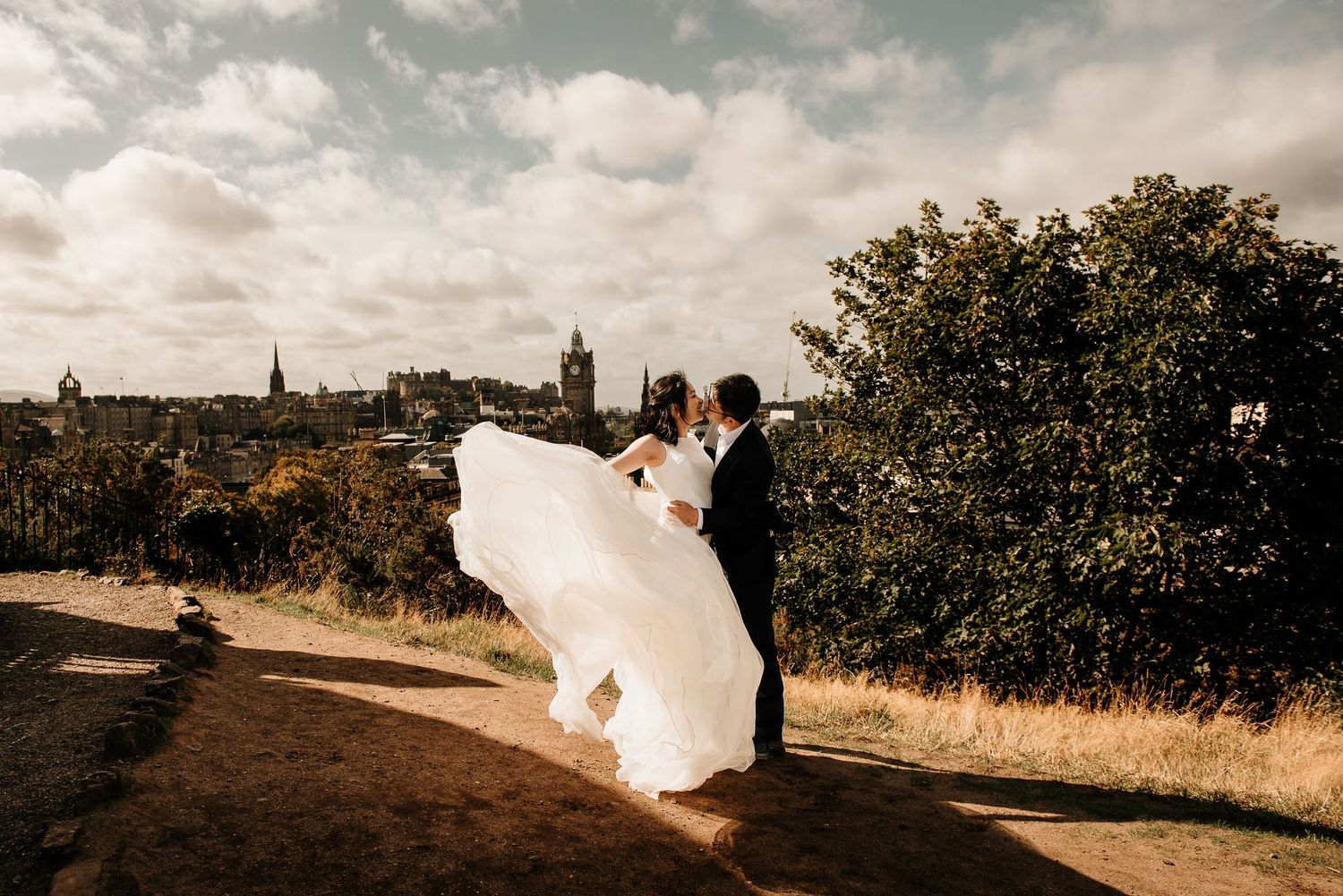 Wedding veil flowing dramatically against cloudy sky in panoramic view.