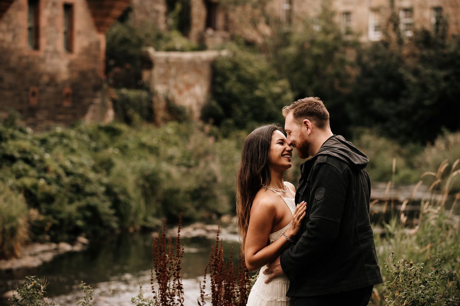 A couple shares an intimate moment against a rustic stone building backdrop.