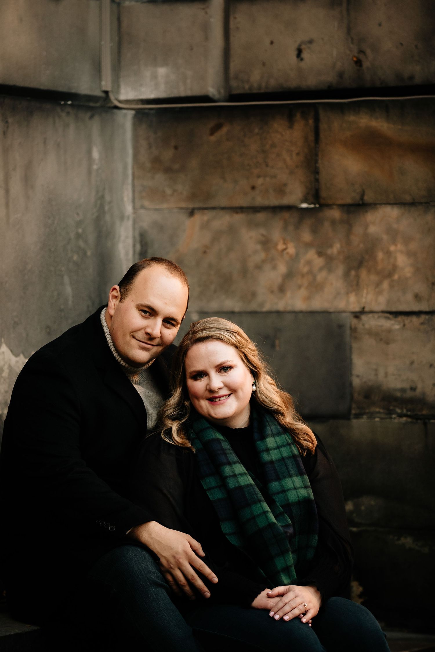 Romantic couple in dark moody setting wearing black and green plaid clothing share intimate moments in dramatic lighting.