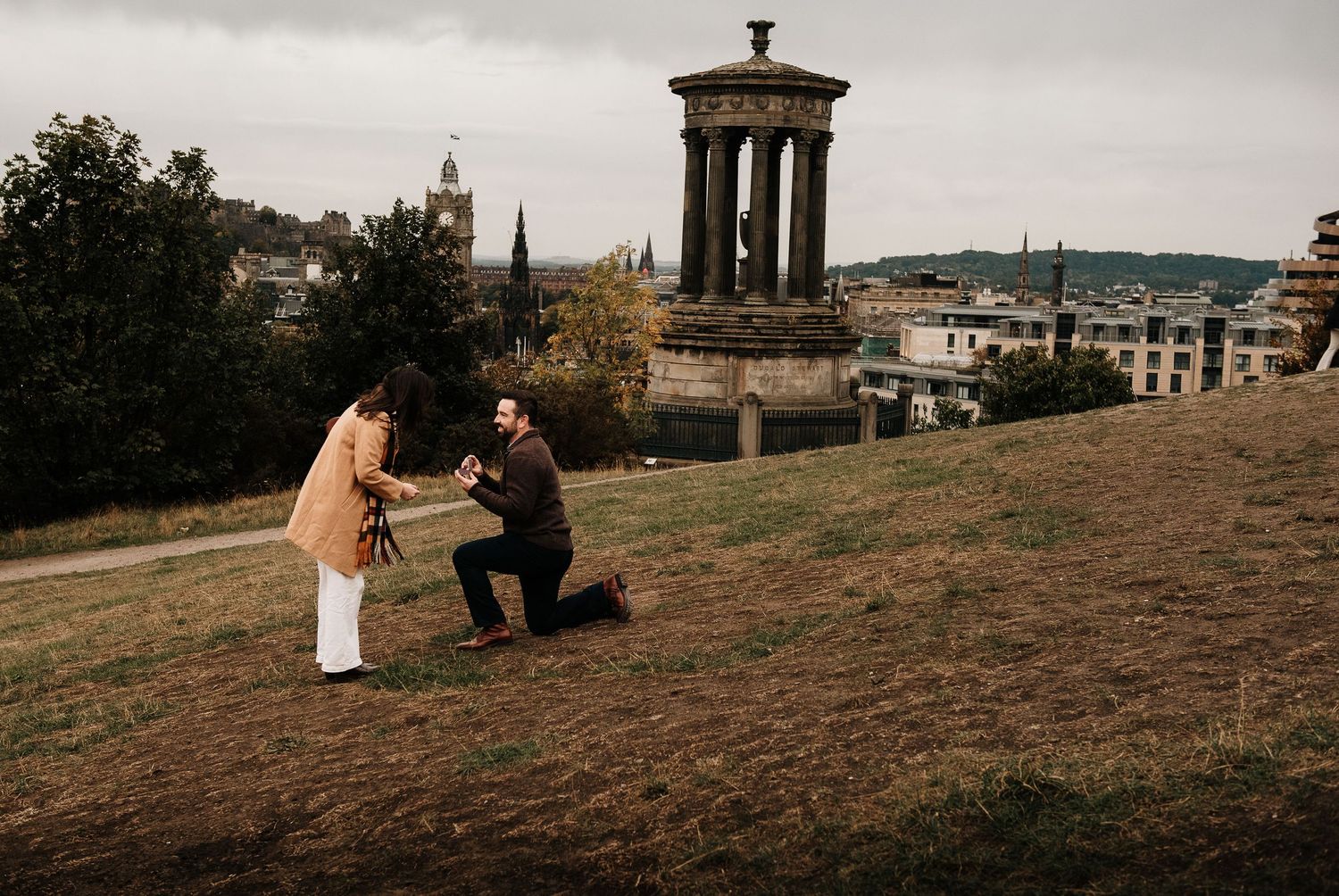 A proposal moment at Edinburgh's Calton Hill with the city skyline in the background.