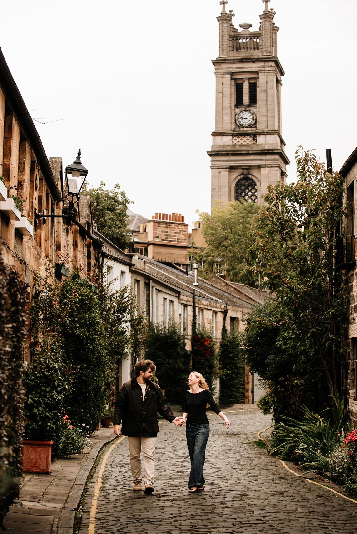 Historic Edinburgh street with stone buildings and church spire on an overcast day.