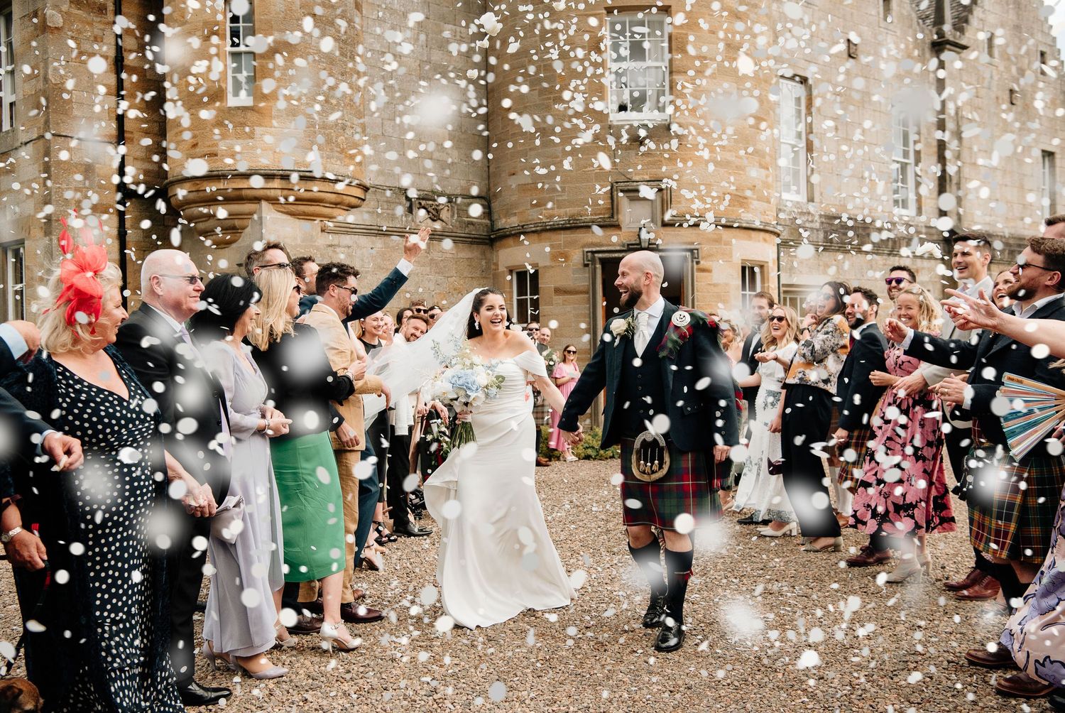 Wedding celebration with guests throwing confetti in front of a stone wall.