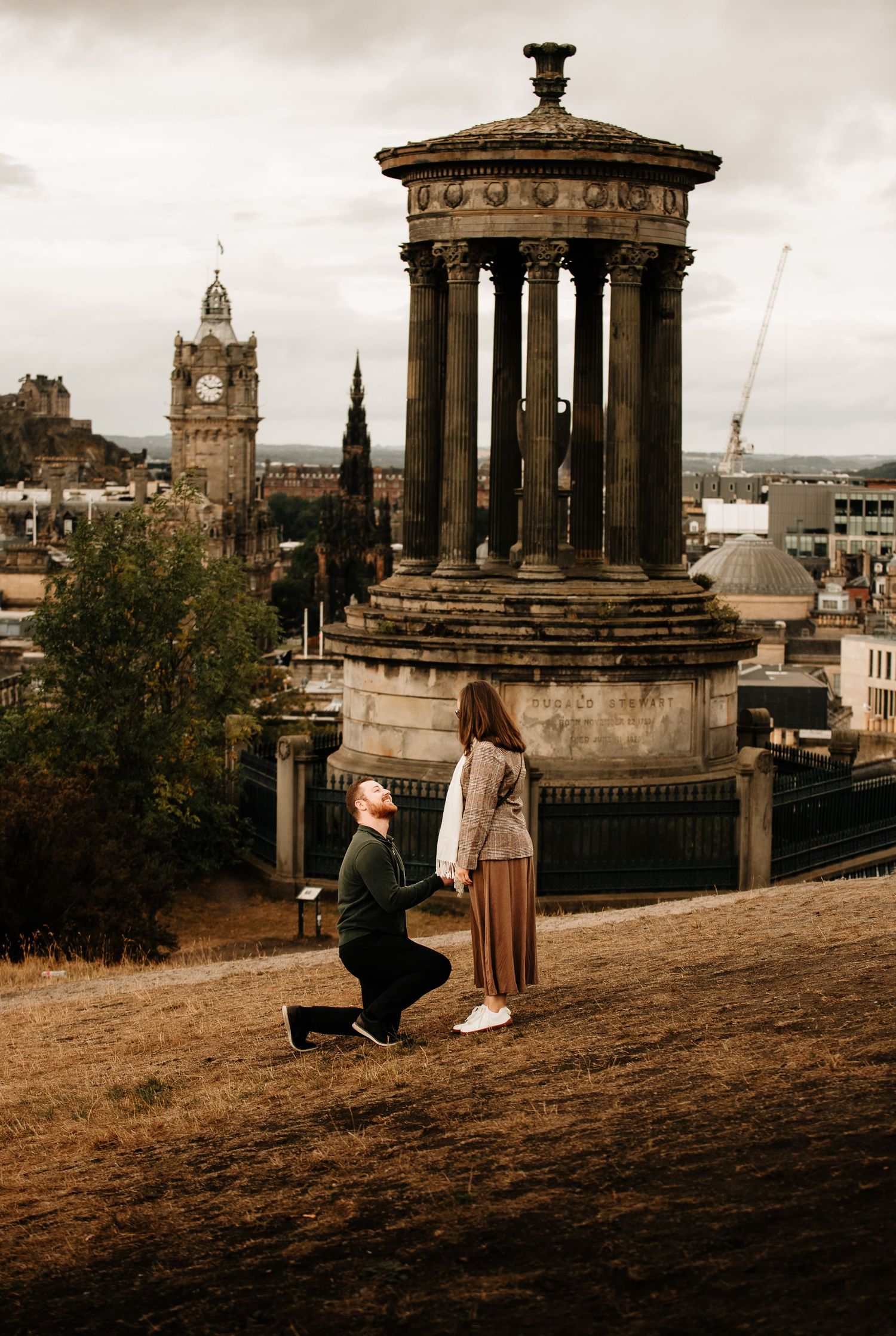 Couple sharing a special moment at Edinburgh's Calton Hill with historic monuments and city views.