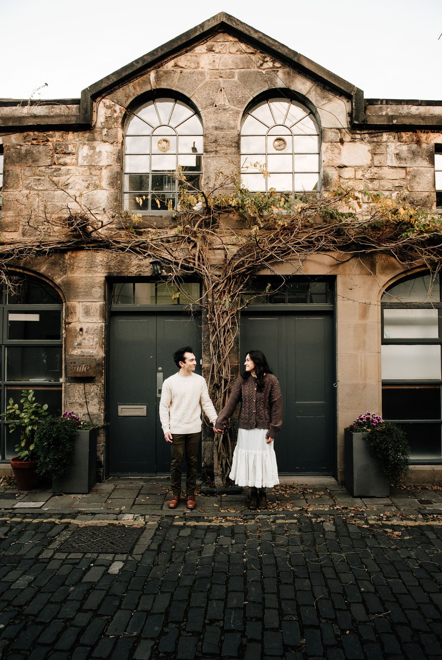 Historic stone buildings with dark doors and arched windows line a cobblestone street.