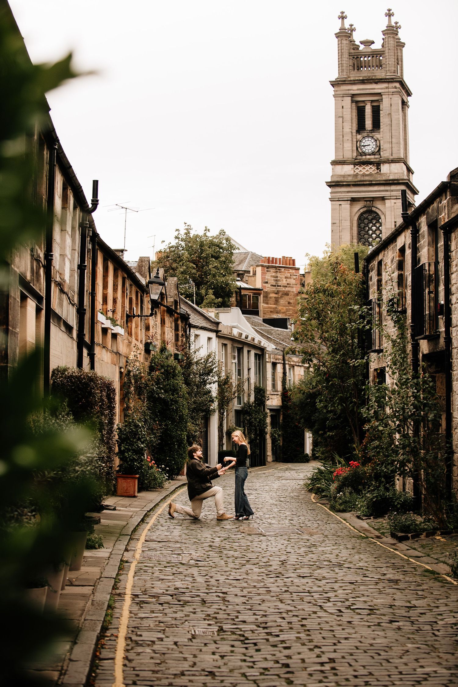 Scenic cobblestone street with traditional Scottish architecture and church tower in autumn.