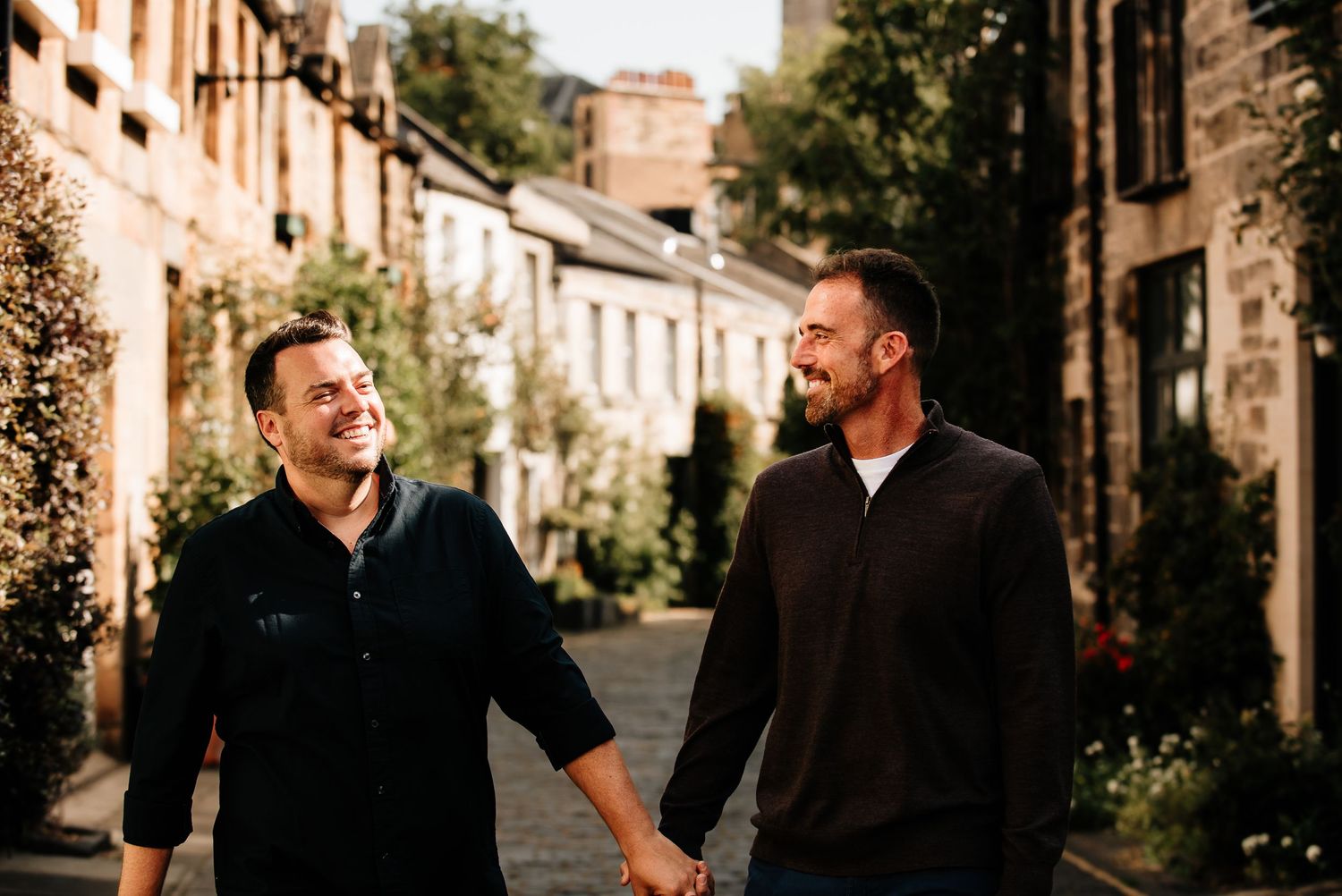 Couple laughing together on a charming cobblestone street lined with historic buildings.