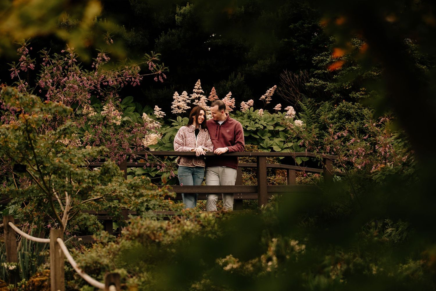 Couple sharing an intimate moment on a wooden bridge surrounded by blooming gardens.