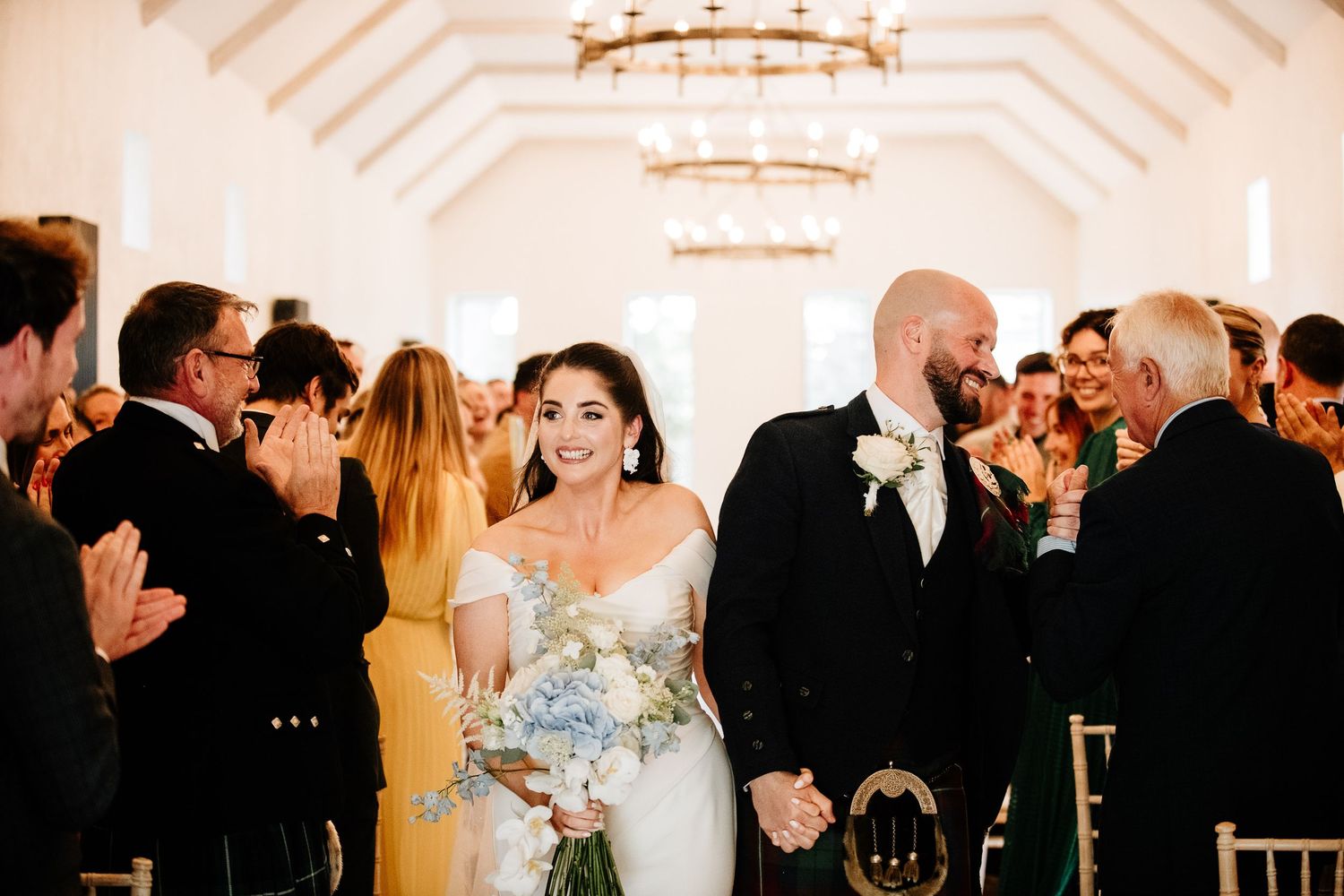 Indoor wedding reception with guests dancing under elegant chandeliers.