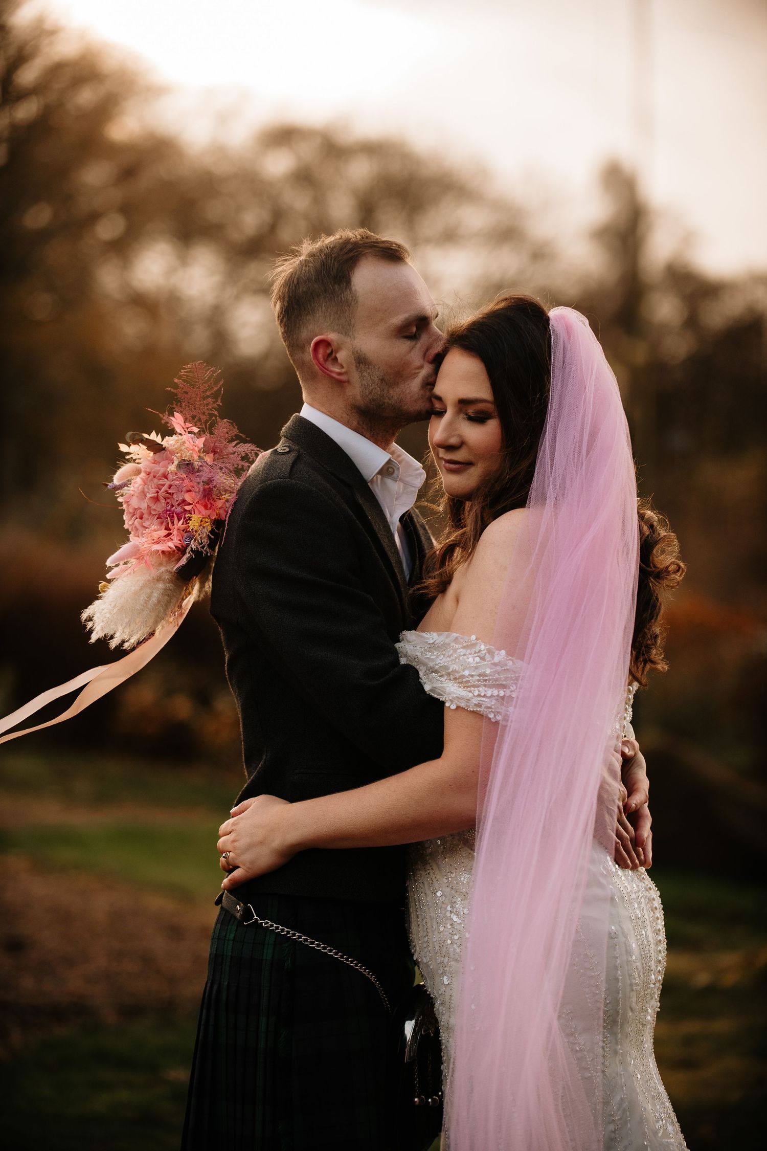 Couple shares tender moments during sunset wedding photoshoot with pink veil.