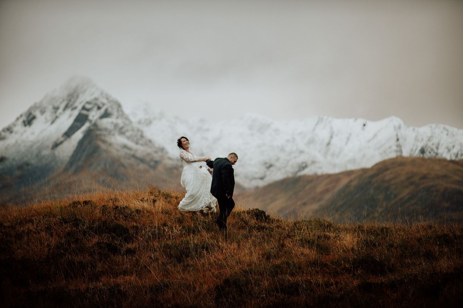 Wedding couple embraces against dramatic mountain landscape at sunset.