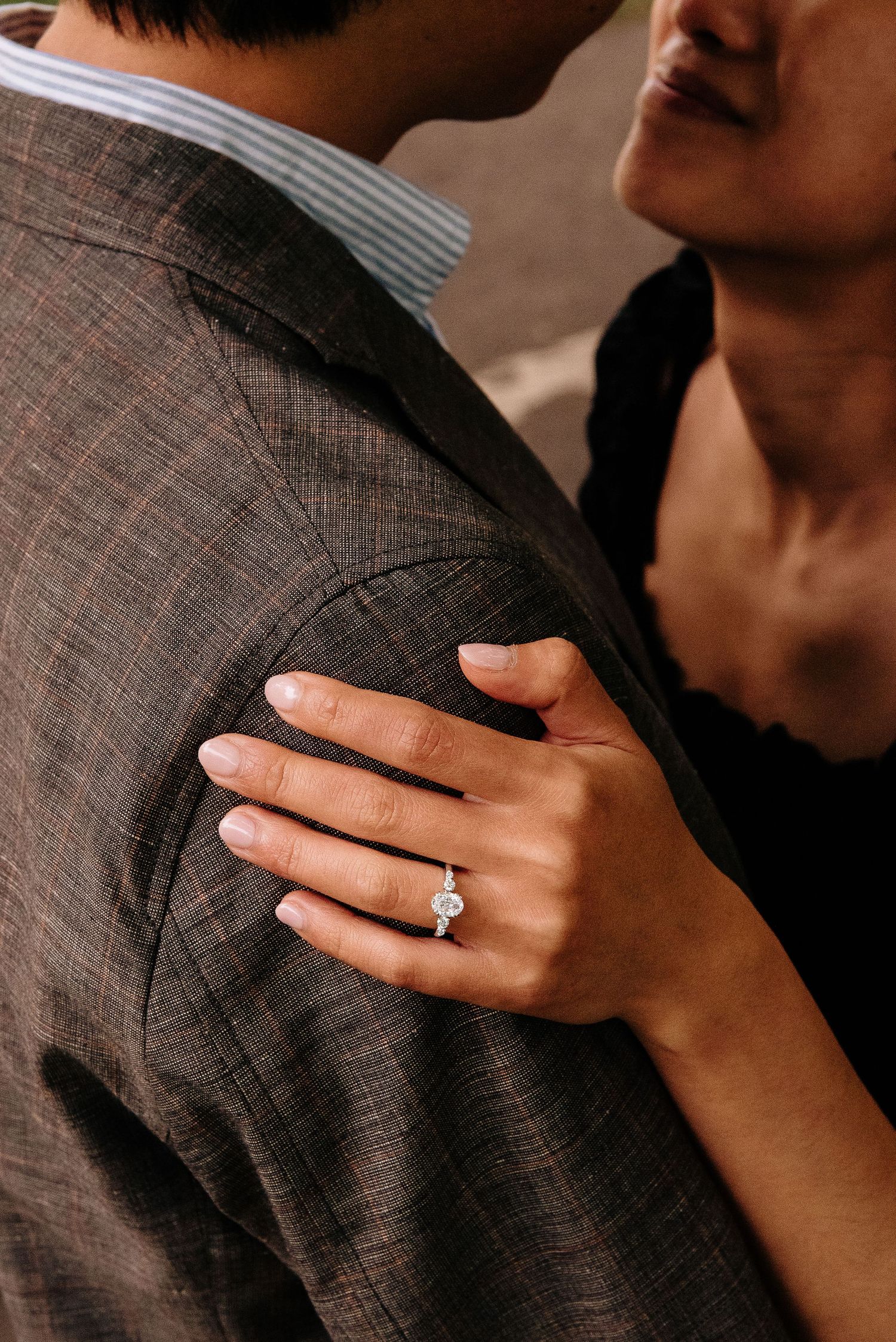 Close-up shots of hands embracing with a sparkling engagement ring on display against a dark suit background.