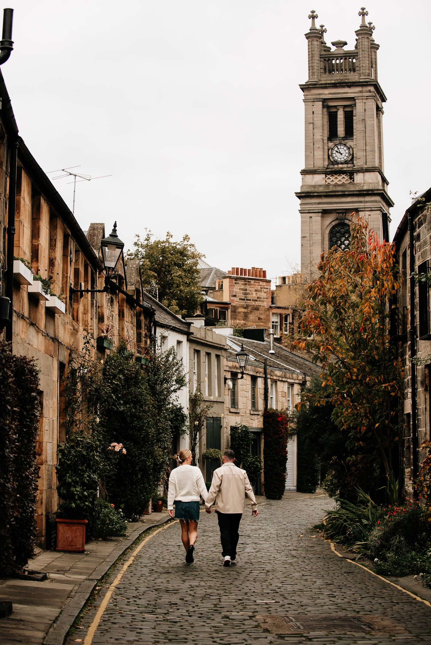 People stroll down a picturesque cobblestone lane with historic architecture in Edinburgh.