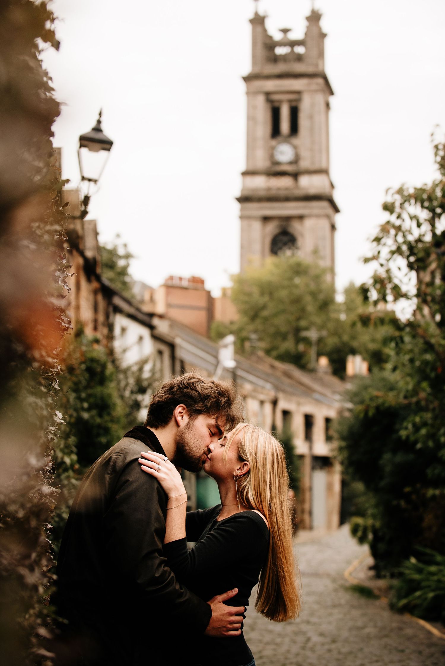 Intimate moment on a cobblestone street with church tower in background.