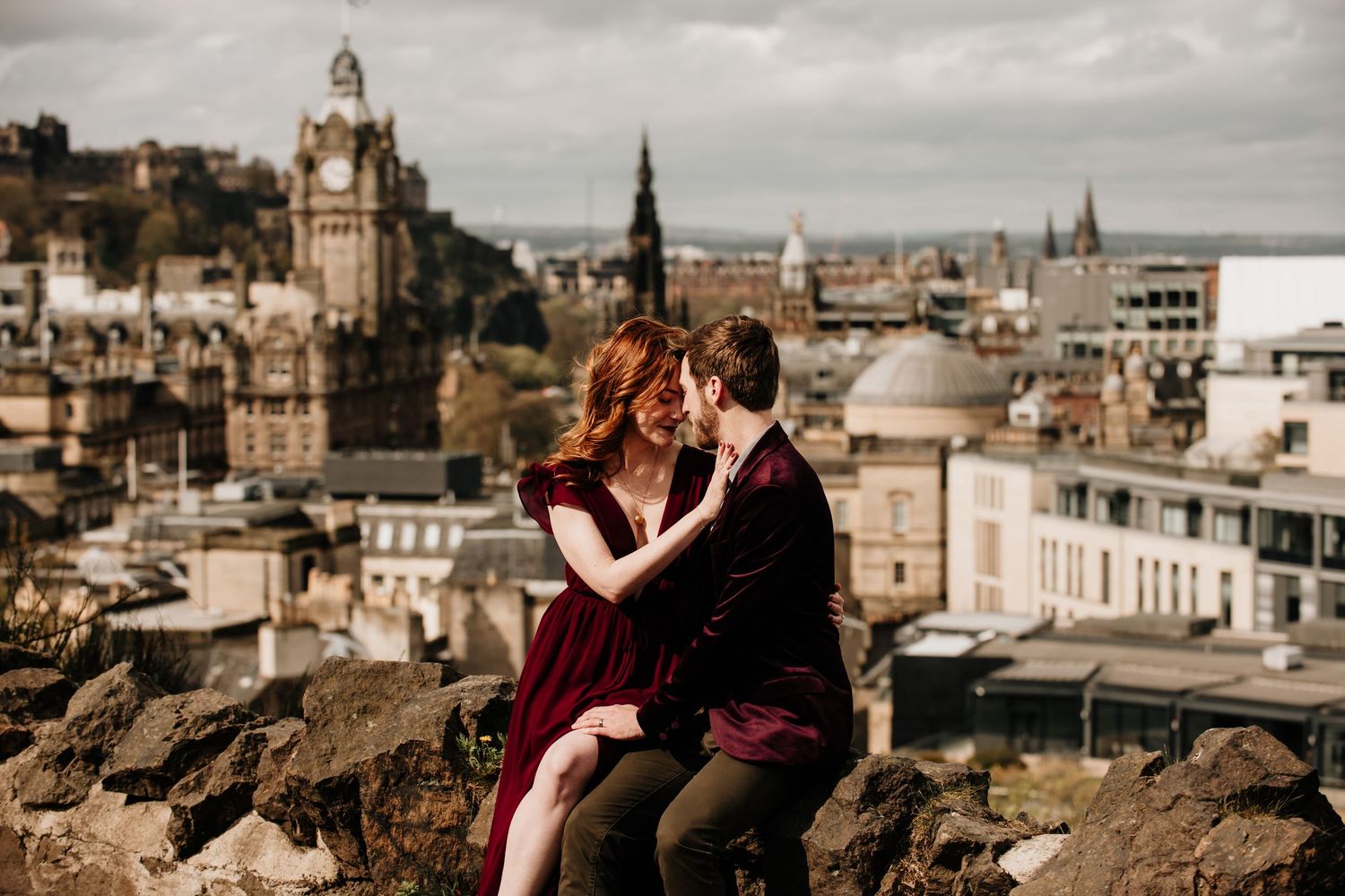Romantic couple embraces against Edinburgh's historic skyline with church spires and historic architecture in view.