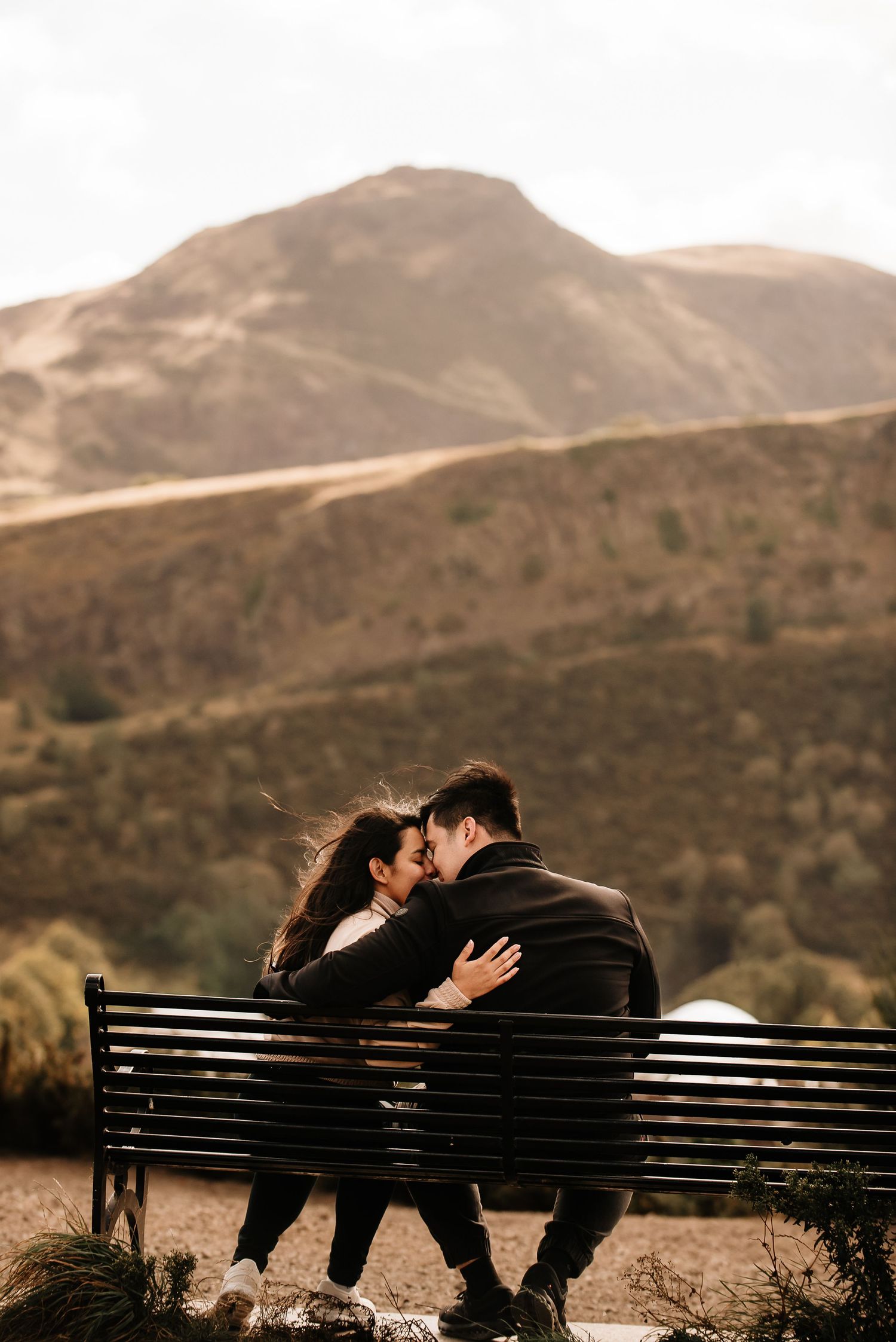 Silhouetted couple sharing a romantic moment on a bench against mountainous backdrop at sunset.